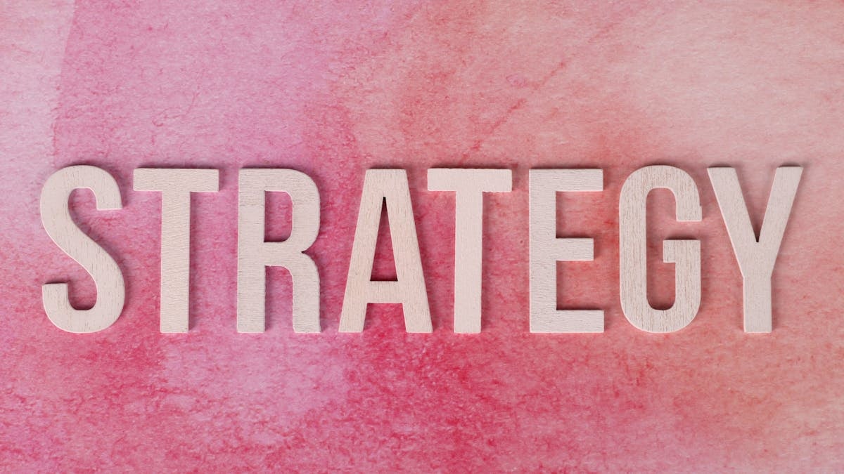 Wooden letters spelling 'Strategy' on a pink textured background.